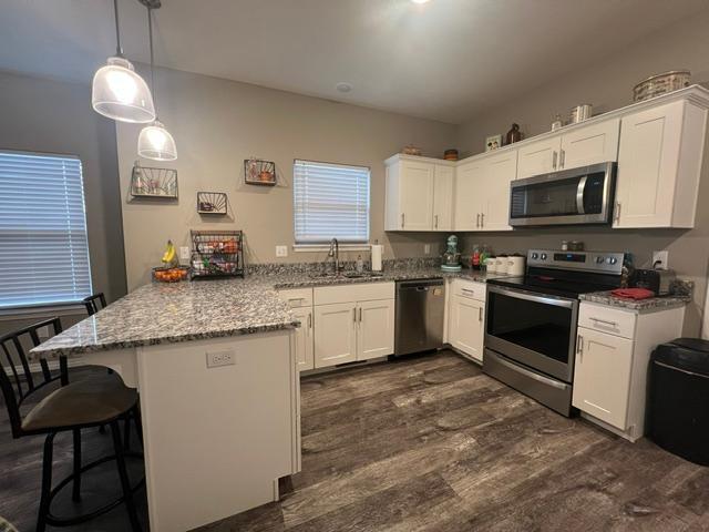 kitchen with stainless steel appliances, decorative light fixtures, kitchen peninsula, and white cabinets