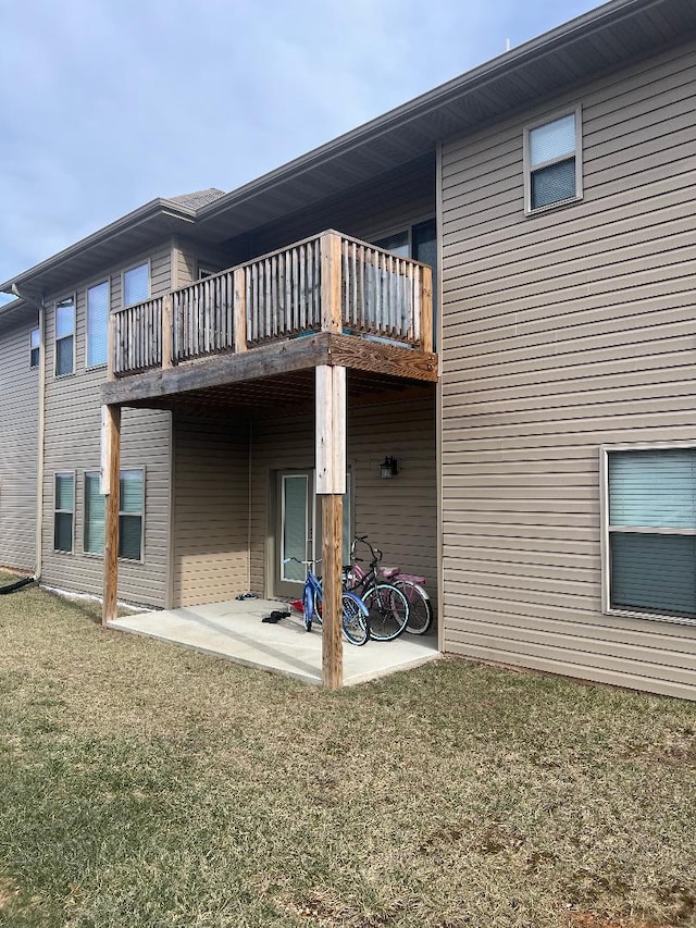 rear view of property featuring a patio area, a balcony, and a lawn