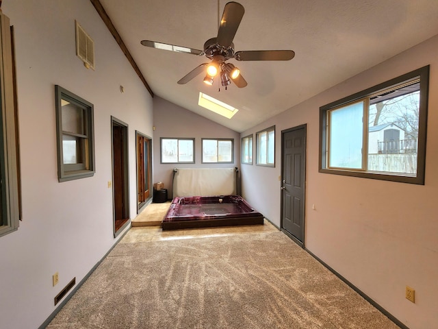 unfurnished bedroom with ceiling fan, vaulted ceiling with skylight, and light carpet