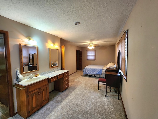 bedroom featuring sink, built in desk, light colored carpet, a textured ceiling, and ceiling fan