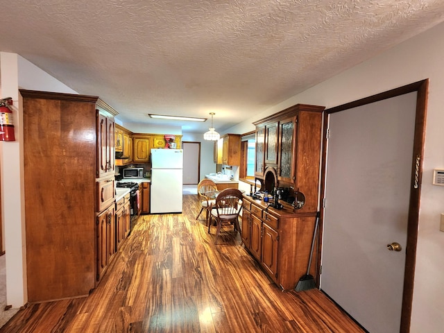 kitchen featuring pendant lighting, range with gas stovetop, white refrigerator, dark wood-type flooring, and a textured ceiling