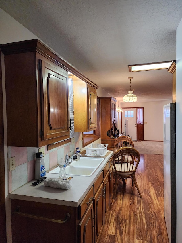 kitchen featuring dark wood-type flooring, sink, decorative light fixtures, a textured ceiling, and backsplash