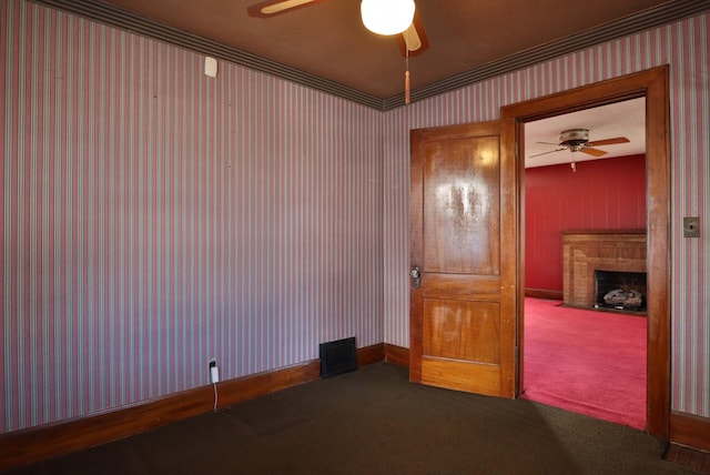 carpeted empty room featuring wallpapered walls, baseboards, visible vents, a ceiling fan, and a fireplace