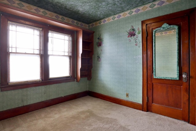 unfurnished room with light colored carpet, a textured ceiling, baseboards, and wallpapered walls