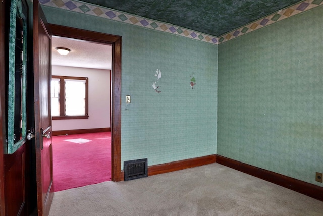 unfurnished room with a textured ceiling, visible vents, baseboards, carpet, and wallpapered walls