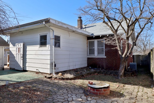 back of house featuring brick siding, a chimney, central AC, fence, and a fire pit