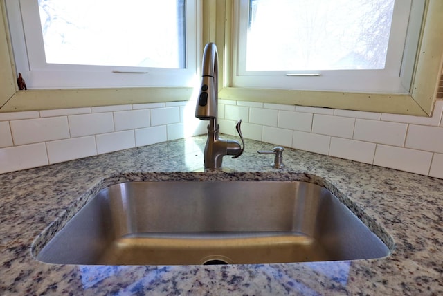 room details featuring light stone countertops, backsplash, and a sink