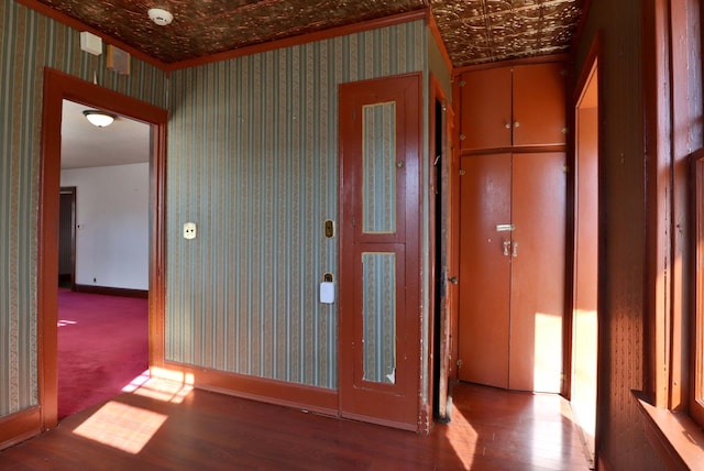 corridor with wallpapered walls, an ornate ceiling, baseboards, and wood finished floors