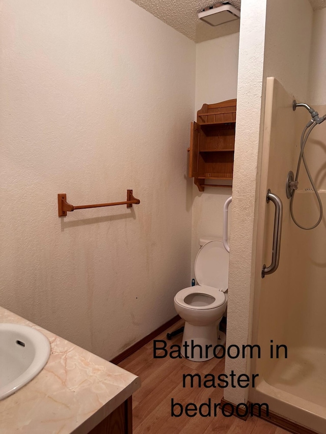 bathroom with hardwood / wood-style flooring, vanity, walk in shower, toilet, and a textured ceiling