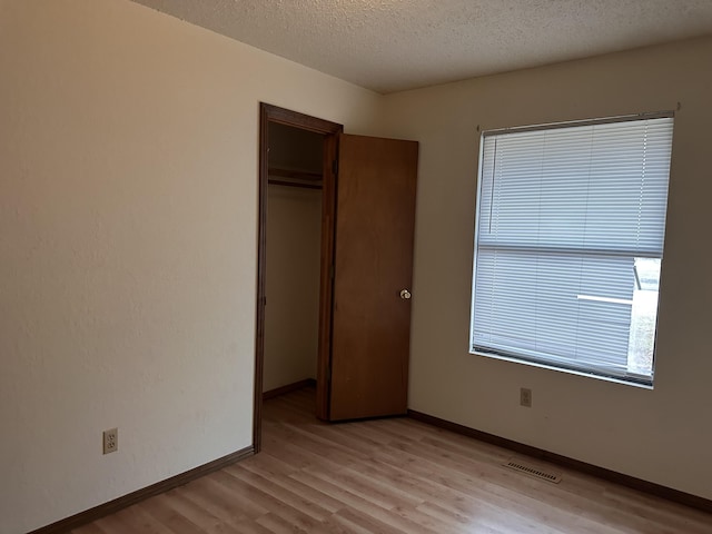 unfurnished bedroom with a textured ceiling, light wood-type flooring, and a closet