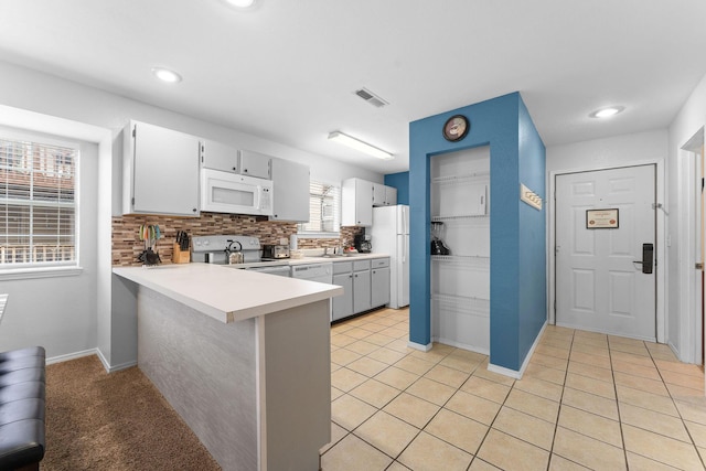 kitchen with white appliances, a breakfast bar area, light tile patterned flooring, decorative backsplash, and kitchen peninsula