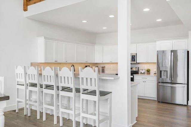 kitchen featuring a breakfast bar, white cabinetry, tasteful backsplash, dark hardwood / wood-style floors, and stainless steel appliances