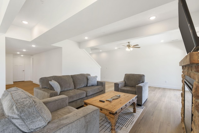 living room featuring ceiling fan, a fireplace, and light wood-type flooring