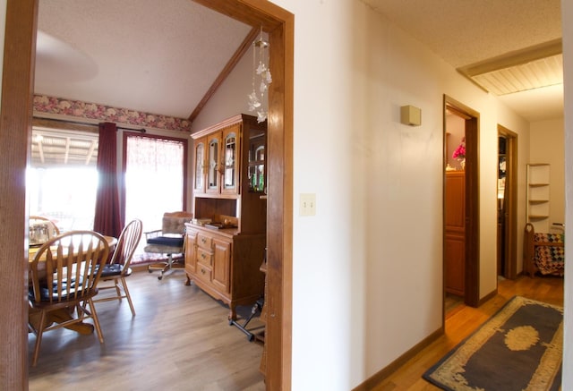 hallway featuring lofted ceiling, a textured ceiling, and light hardwood / wood-style flooring