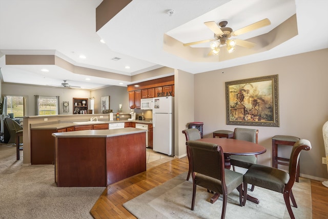 kitchen with white appliances, a tray ceiling, kitchen peninsula, and sink