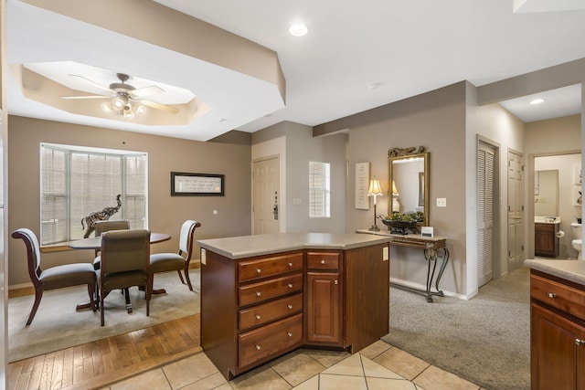 kitchen featuring ceiling fan, light colored carpet, a center island, and a raised ceiling