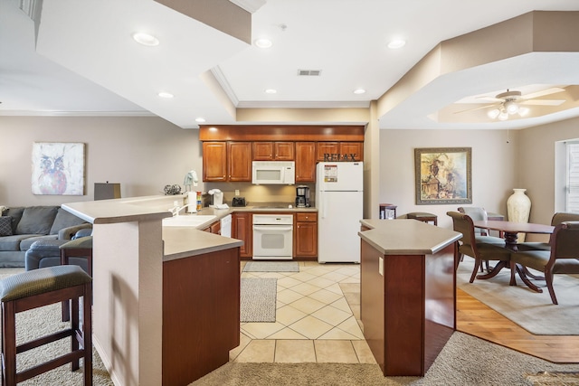 kitchen featuring a breakfast bar, white appliances, kitchen peninsula, a raised ceiling, and ceiling fan