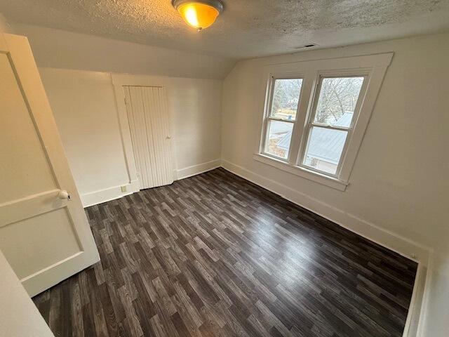 unfurnished bedroom with dark hardwood / wood-style floors, vaulted ceiling, and a textured ceiling