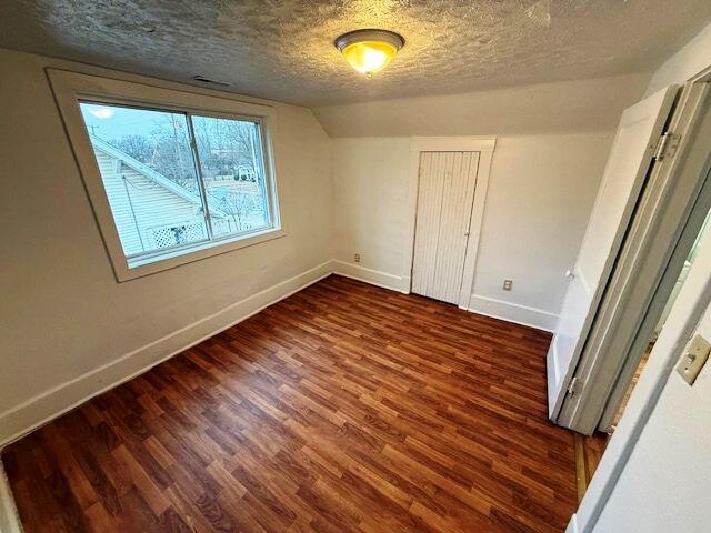 unfurnished bedroom featuring lofted ceiling, dark hardwood / wood-style floors, a textured ceiling, and a closet