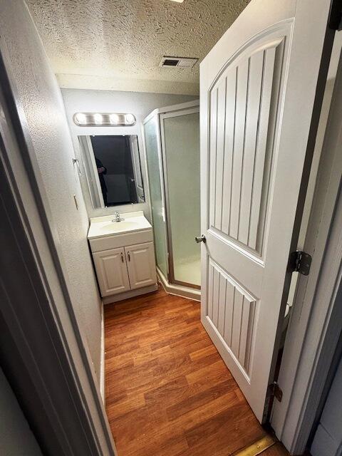 bathroom featuring vanity, hardwood / wood-style flooring, a textured ceiling, and walk in shower