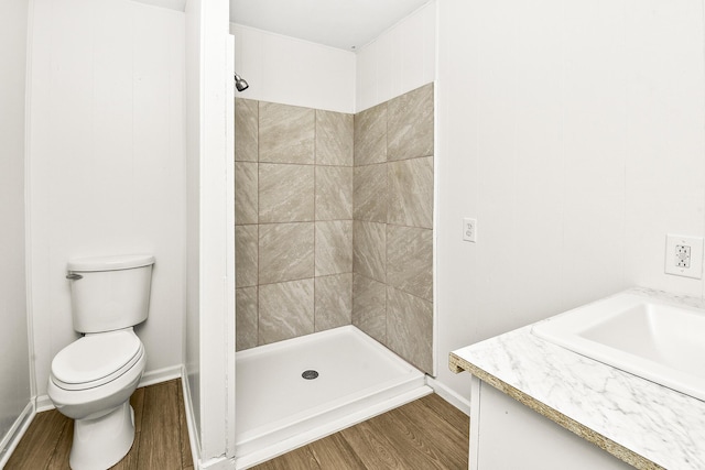 bathroom featuring vanity, tiled shower, hardwood / wood-style floors, and toilet