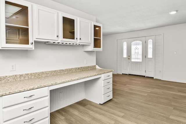 kitchen featuring white cabinetry, built in desk, light hardwood / wood-style floors, and a textured ceiling