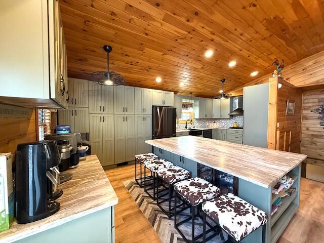 kitchen featuring a kitchen island, hanging light fixtures, fridge, light hardwood / wood-style floors, and wall chimney range hood