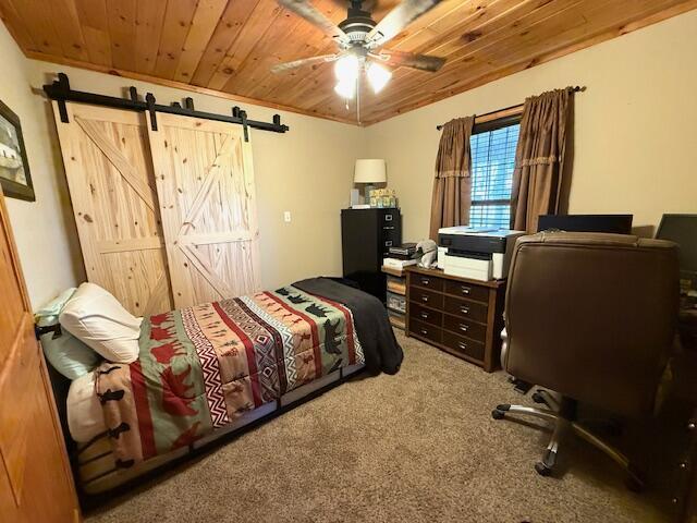 bedroom with wood ceiling, ceiling fan, a barn door, and carpet floors