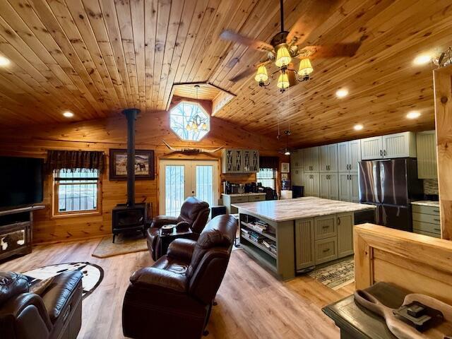 interior space with vaulted ceiling, wooden walls, a wood stove, wood ceiling, and light hardwood / wood-style floors