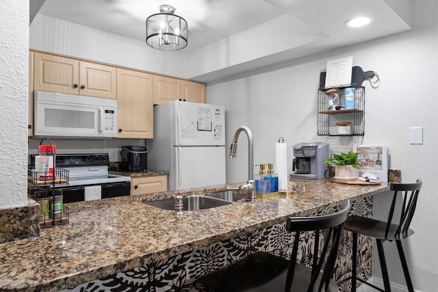 kitchen featuring sink, a kitchen breakfast bar, dark stone counters, light brown cabinets, and white appliances