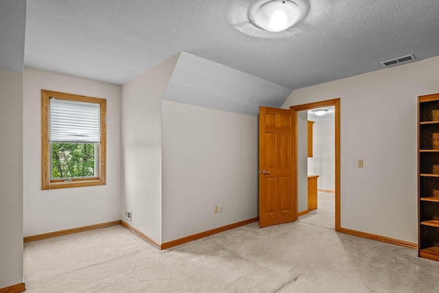 additional living space with light colored carpet, vaulted ceiling, and a textured ceiling