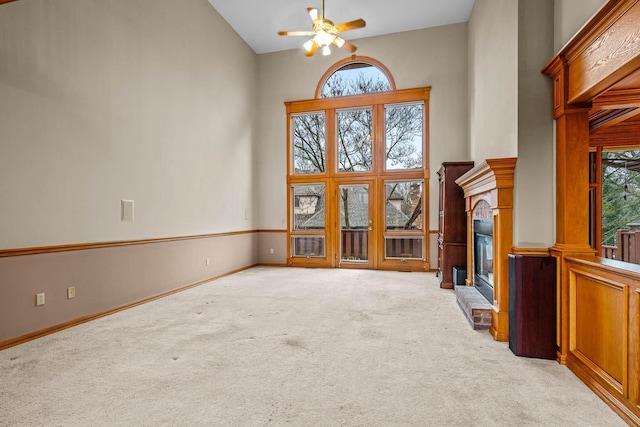 unfurnished living room with light carpet, a towering ceiling, and ceiling fan