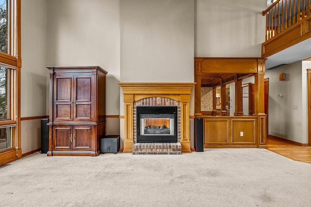 unfurnished living room featuring a towering ceiling, a brick fireplace, and light carpet