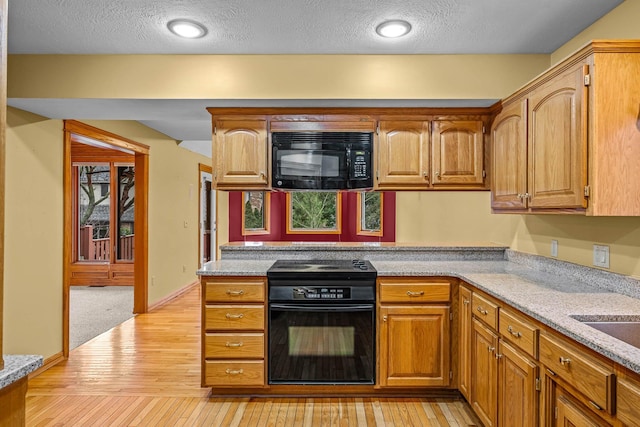 kitchen with light stone countertops, stove, a textured ceiling, and light hardwood / wood-style floors