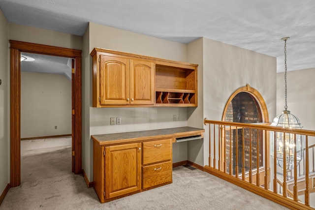 kitchen featuring pendant lighting, built in desk, and light colored carpet