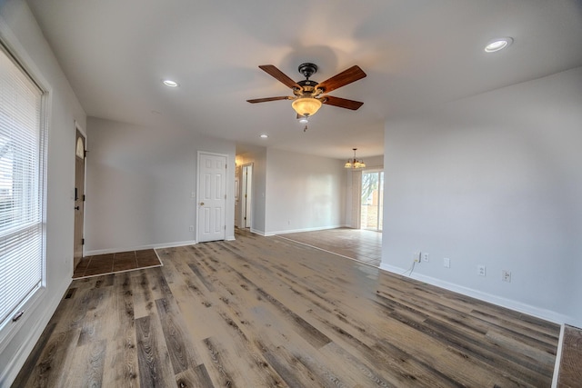 empty room featuring ceiling fan with notable chandelier and hardwood / wood-style floors