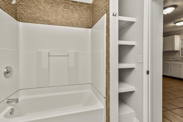 bathroom featuring tile patterned flooring, bathtub / shower combination, and a textured ceiling