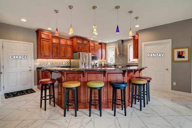 kitchen featuring pendant lighting, wall chimney range hood, stainless steel appliances, a center island, and decorative backsplash