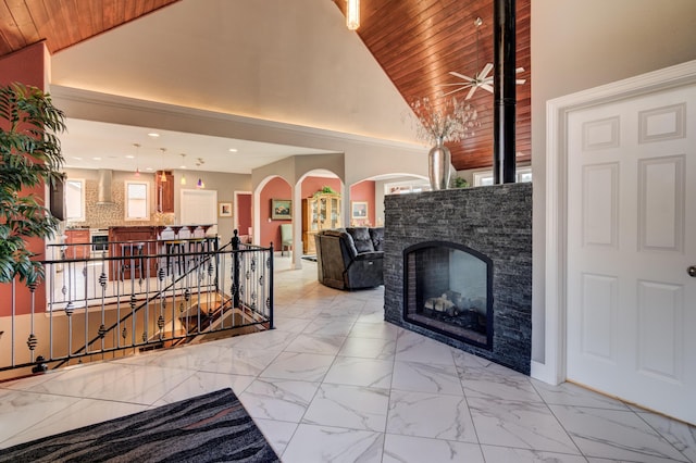 living room with ceiling fan, a stone fireplace, wood ceiling, and high vaulted ceiling