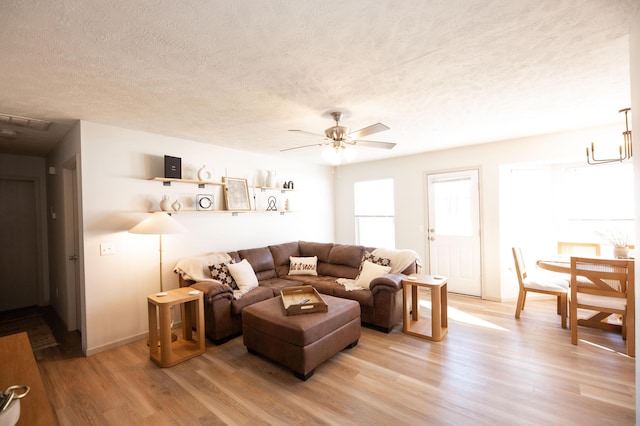 living room featuring ceiling fan with notable chandelier, hardwood / wood-style floors, and a textured ceiling