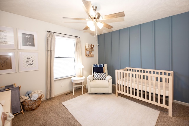 carpeted bedroom featuring a nursery area and ceiling fan