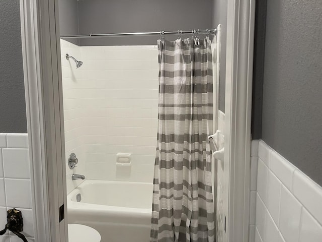 bathroom featuring toilet, wainscoting, shower / bath combination with curtain, and tile walls