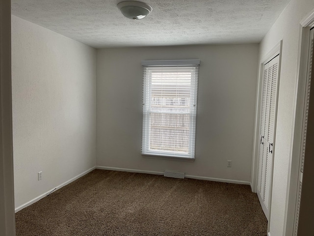 unfurnished room with a textured ceiling and dark carpet