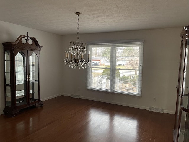 unfurnished dining area with baseboards, visible vents, dark wood-type flooring, an inviting chandelier, and a textured ceiling