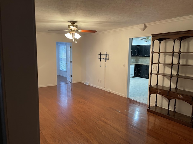 spare room with a textured ceiling, ceiling fan, wood finished floors, and crown molding