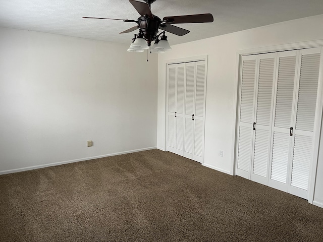 unfurnished bedroom with carpet flooring, two closets, a textured ceiling, and ceiling fan