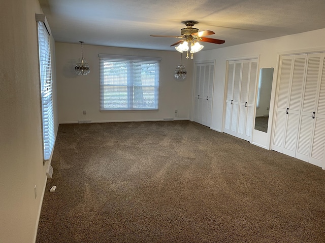 unfurnished bedroom with multiple closets, ceiling fan, and dark colored carpet