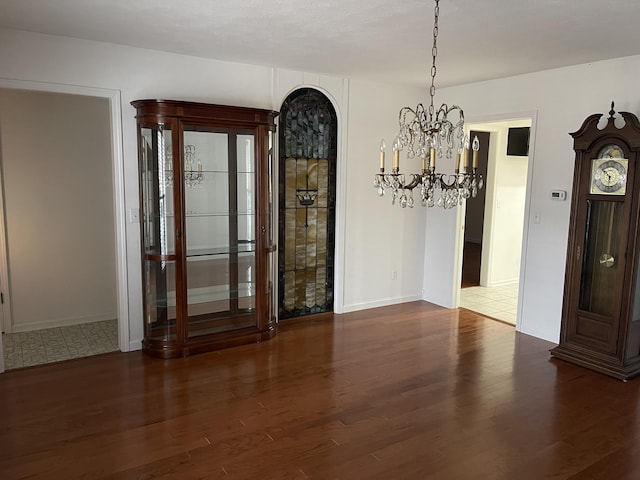 unfurnished dining area featuring dark wood-type flooring, a notable chandelier, and baseboards