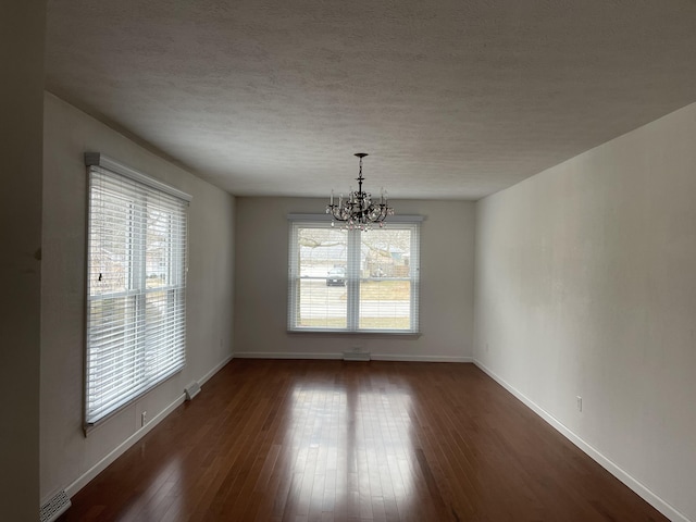 spare room with an inviting chandelier, dark wood-type flooring, and a textured ceiling