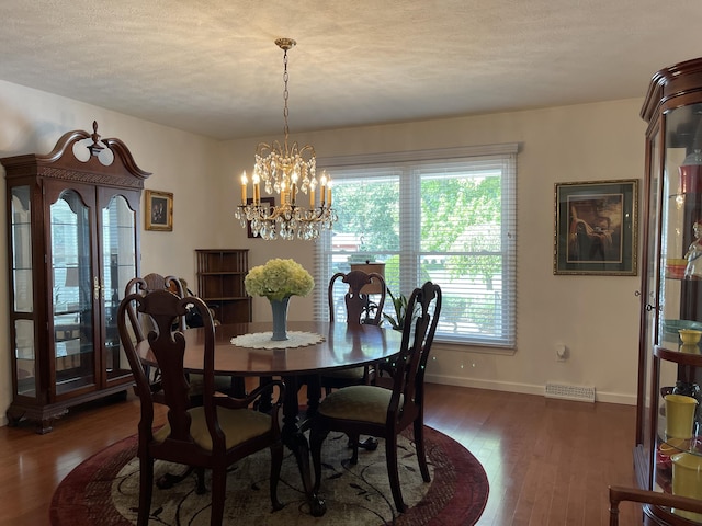 dining space featuring dark wood finished floors, visible vents, a textured ceiling, a chandelier, and baseboards